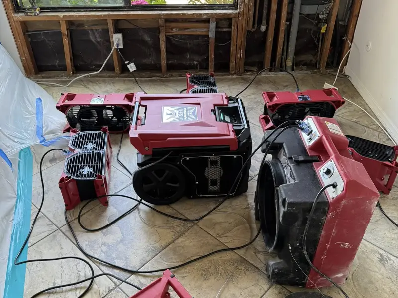 Multiple red industrial air movers and a dehumidifier arranged on a tiled floor in a room under renovation. water damage restoration