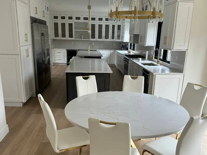 Modern kitchen with white cabinets, two islands, and a round marble dining table with six white chairs. Done by experienced restoration company in San Diego