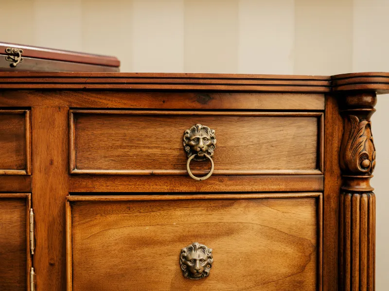 Close-up of a wooden cabinet drawer with a lion head metal handle and decorative carved corner. contents cleaning and restoration